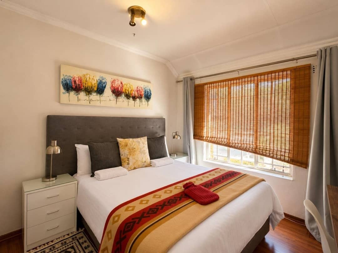 Bedroom with a grey upholstered headboard, patterned throw, bamboo blind and wooden floor