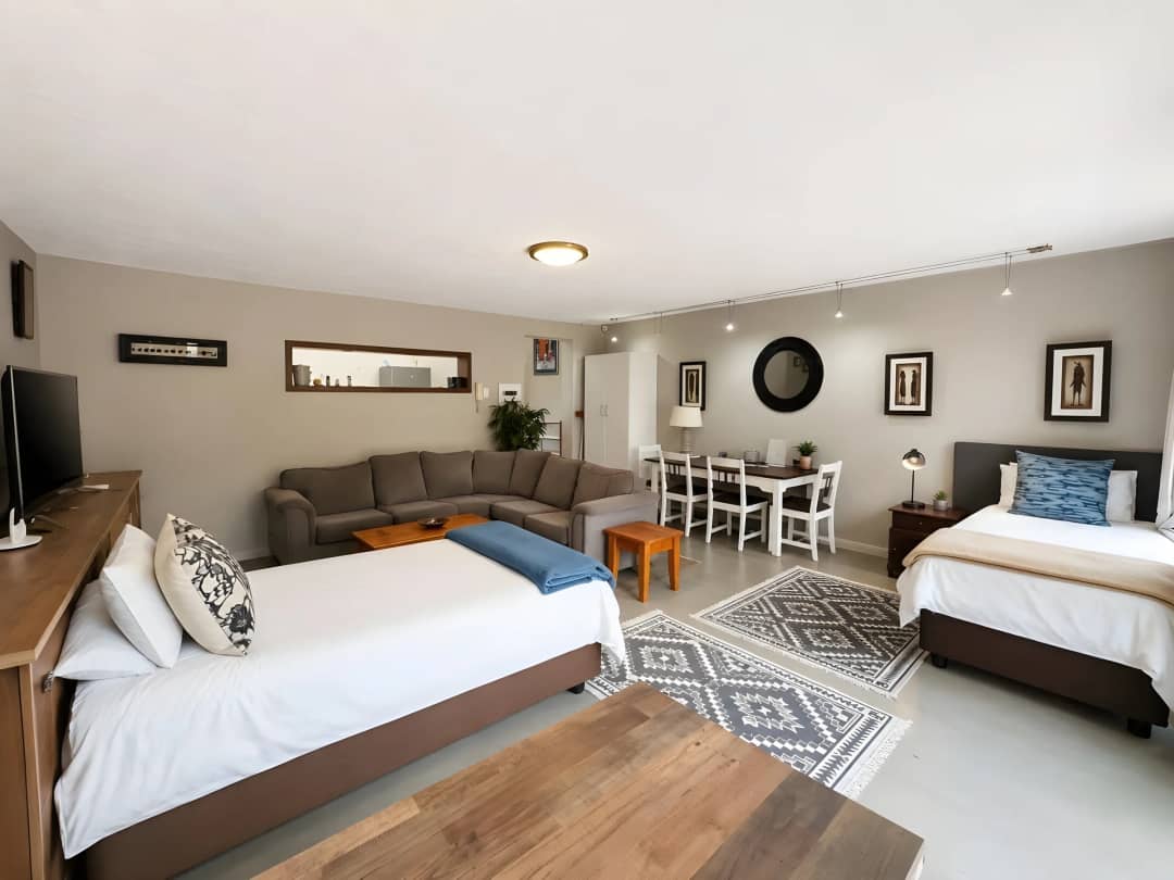 Open-plan studio with two beds, a corner sofa, dining table and wall-mounted TV