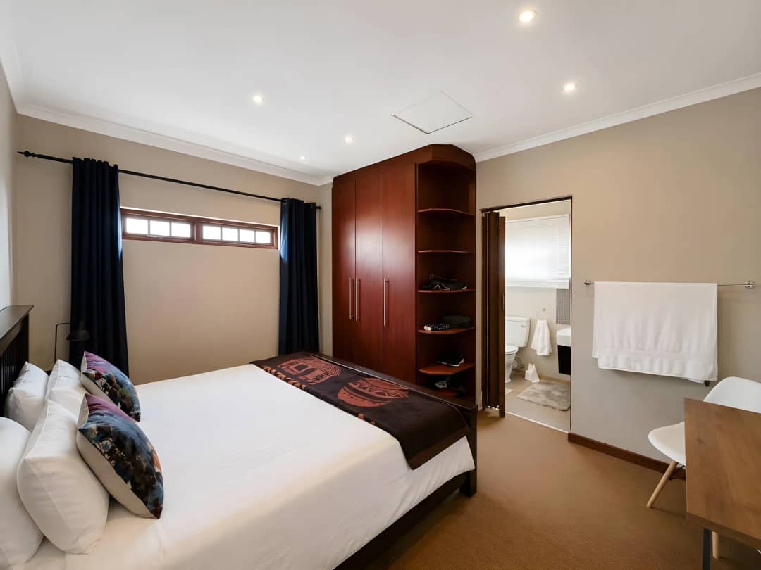 Bedroom with mahogany built-in cupboards and corner shelving, opening into an en-suite bathroom