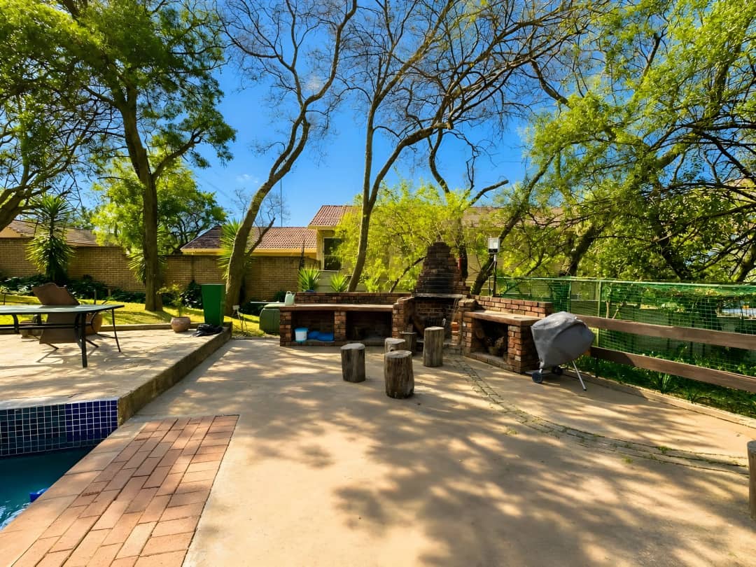 Garden braai area with a built-in brick barbecue, tree-shaded seating and the pool edge in the foreground