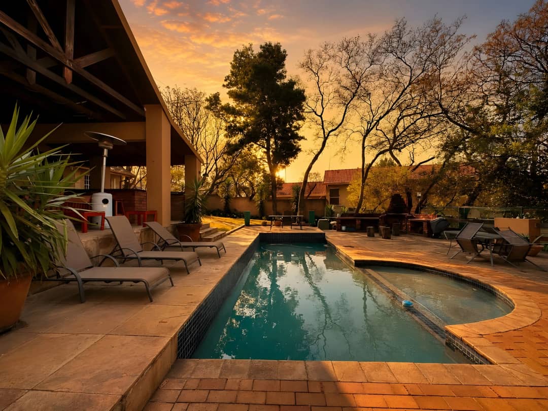 Swimming pool at sunset seen from the covered patio, with sun loungers along the paved edge